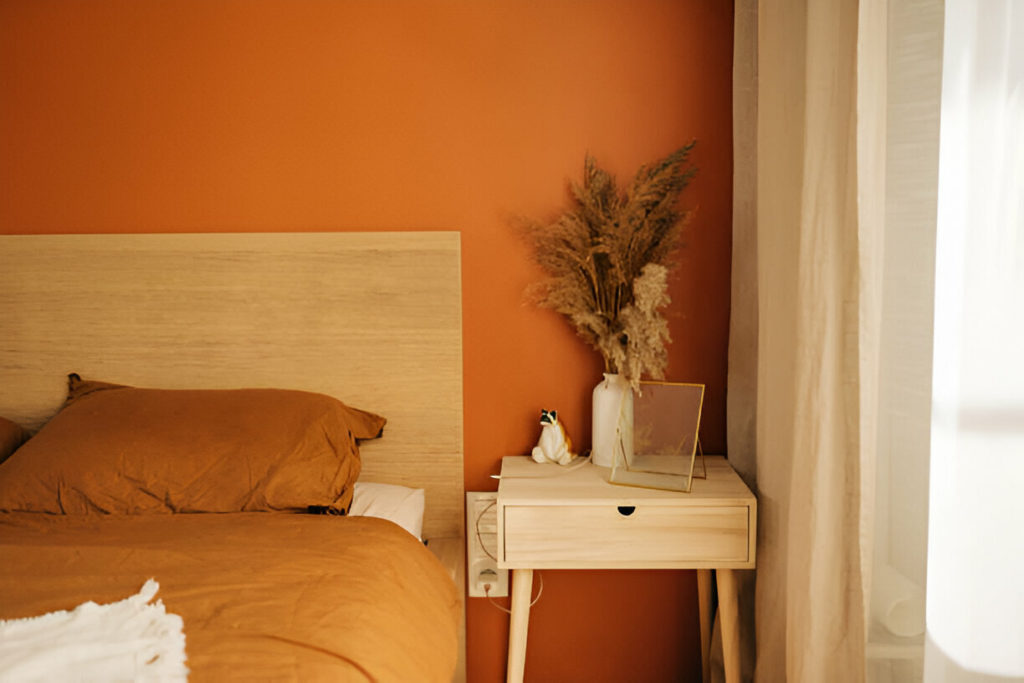 Close-up on simple, white bedside table with decorations next to comfortable bed in bedroom with dark blue wall